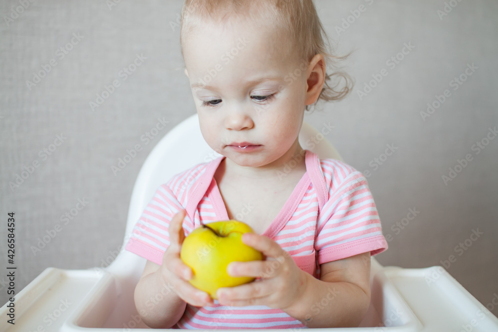 A little girl tastes, examines and plays with fresh apples with pleasure and interest. High quality photo