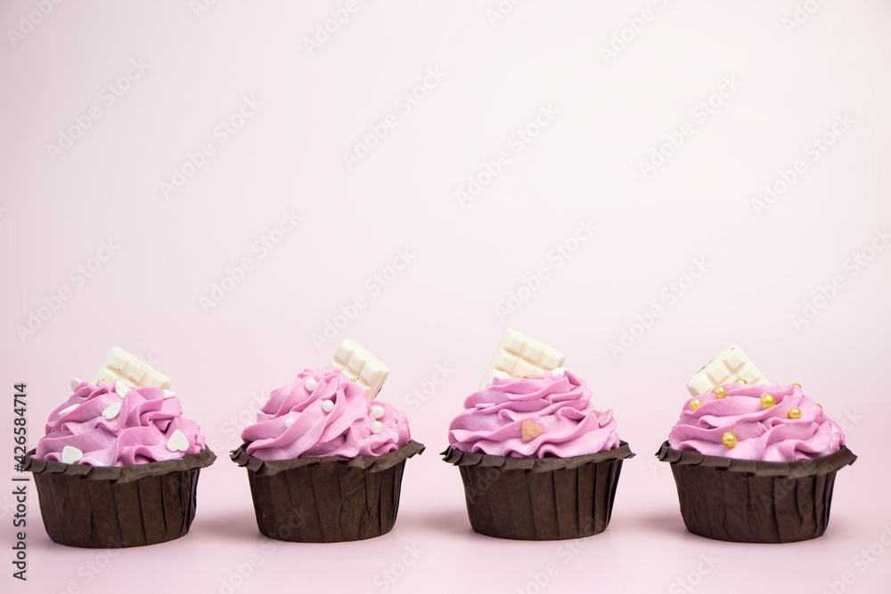 Set of 4 cupcakes with pink berry cream decorated with beads and white chocolate on pink background with copy space for text . Set of 4 cupcakes with pink berry cream decorated with beads and white chocolate on pink background with copy space for text .