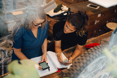 High angle view of female colleagues discussing over smart phone in retail store