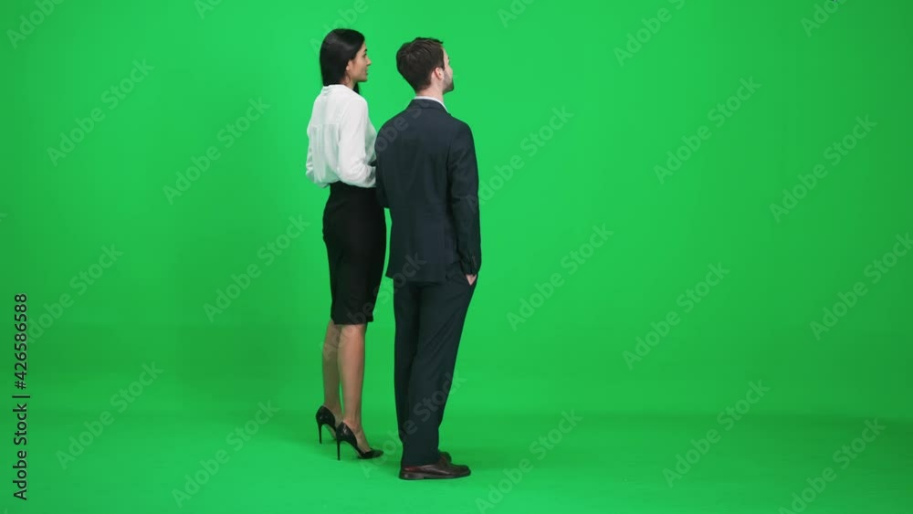 Man and woman in suits stands in the green space of the chromakey, they discuss subjects while looking in front of them, a template on a green background, back view. Man and woman in suits stands in the green space of the chromakey, they discuss subjects while looking in front of them, a template on a green background, back view.