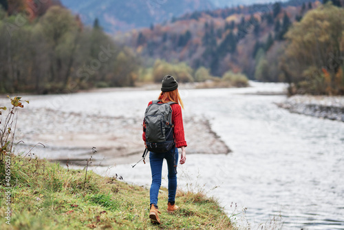 woman hiker with raised hands on the river bank in the mountains in autumn on nature