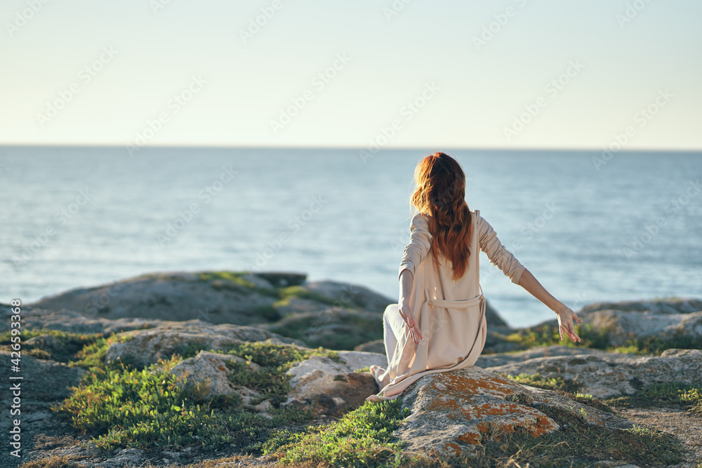 travel woman in sweater sits on a high stone near the sea in the mountains back view