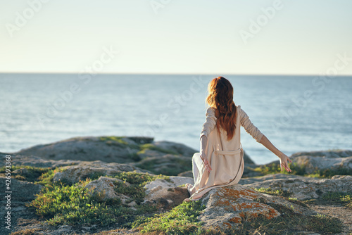 travel woman in sweater sits on a high stone near the sea in the mountains back view