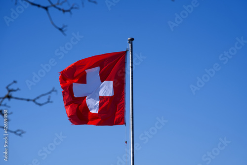 Swiss flag blowing in the wind with blue sky background seen form mountain Bachtel, Zurich, Switzerland. Photo taken April 8th, 2021. photo