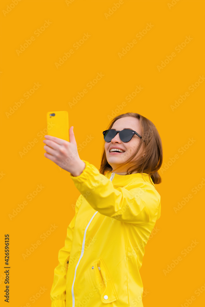 Portrait of attractive girl in summer clothes takes selfie on yellow background, looks into camera and smiles Portrait of attractive girl in summer clothes takes selfie on yellow background, looks into camera and smiles