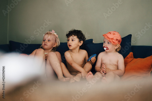 Naked sister by brothers sitting on sofa at home photo