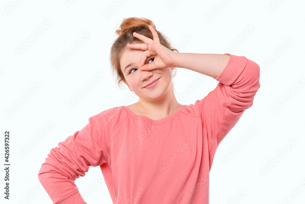Funny young girl in pink casual sweatshirt, showing OK sign over eye and smiling, having faith all be okay Funny young girl in pink casual sweatshirt, showing OK sign over eye and smiling, having faith all be okay