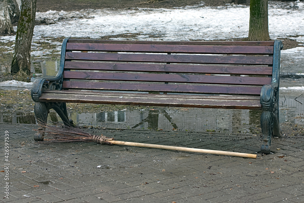 the broom is lying near an old wooden bench the broom is lying near an old wooden bench