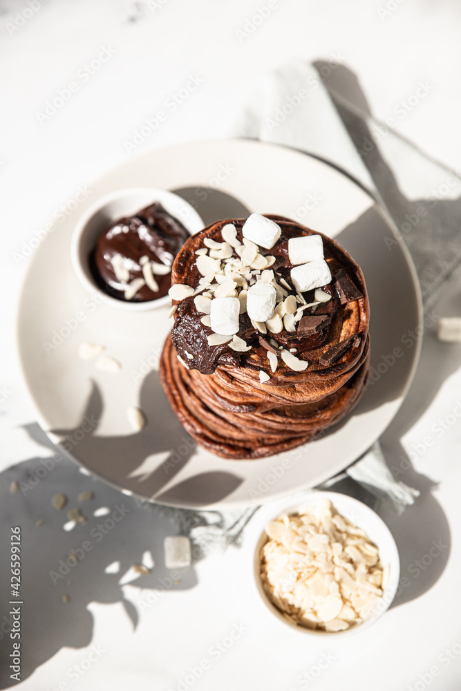 Stack of homemade chocolate pancakes with melted chocolate, ground almond and marshmallow, light background. Direct sunlight and hard shadows. Stack of homemade chocolate pancakes with melted chocolate, ground almond and marshmallow, light background. Direct sunlight and hard shadows.