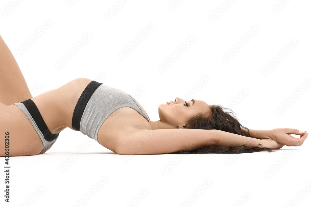 A young attractive brunette girl, in gray underwear, with a fit athletic body, lies in a relaxed position, arched her back. Isolated on white background