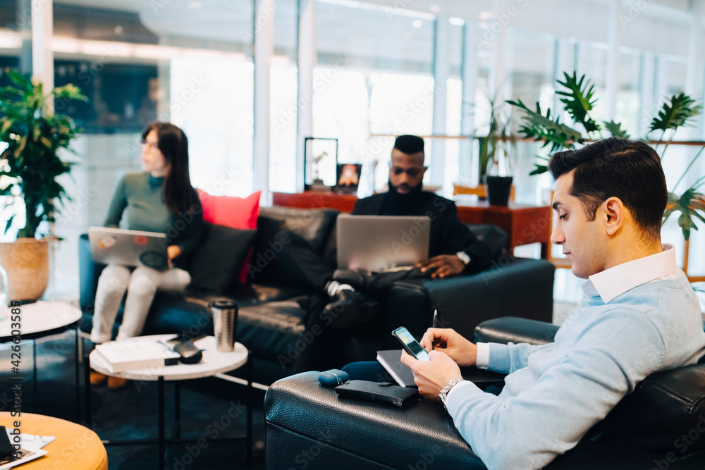 Male entrepreneur using smart phone while working with colleagues in office Male entrepreneur using smart phone while working with colleagues in office