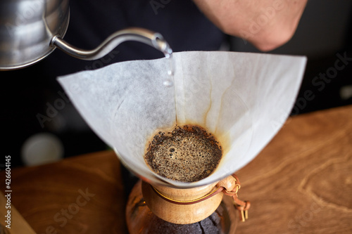 Barista preparing coffee using chemex pour over coffee maker. Alternative ways of brewing coffee. Coffee shop concept. photo