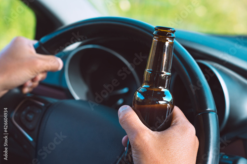 Closeup of drunk driver hands on the steering wheel with a bottle of beer. Driving under alcohol influence