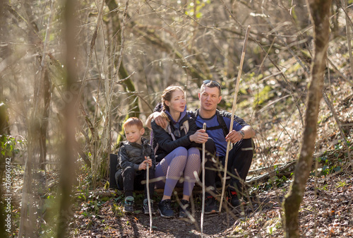 sports family of tourists a man, a woman and a child are sitting resting in the forest on a hike and talking