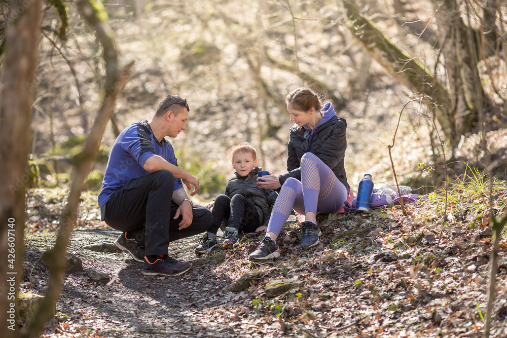 sports family of tourists a man, a woman and a child sit resting in the forest on a hike sports family of tourists a man, a woman and a child sit resting in the forest on a hike