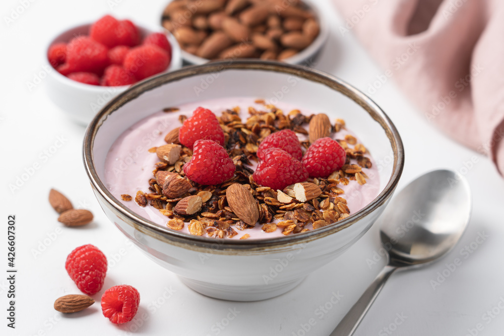 Raspberry yogurt in bowl with granola and almond nuts. Delicious healthy breakfast on white background Raspberry yogurt in bowl with granola and almond nuts. Delicious healthy breakfast on white background