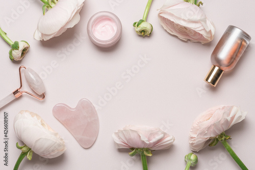 Cosmetics for face and body on pink pastel background with ranuculus flowers. Beauty products for massage, cream, perfume. Monochrome pink color background