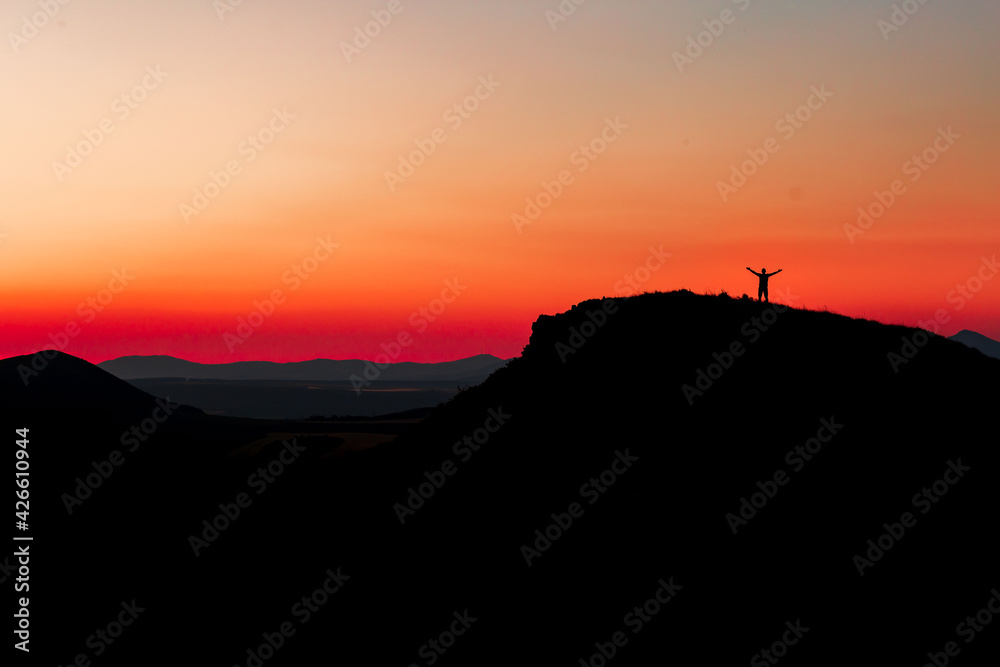 Red sunset with mountain silhouette. A man on mountain in sunset. Traveler on rock waving hands.