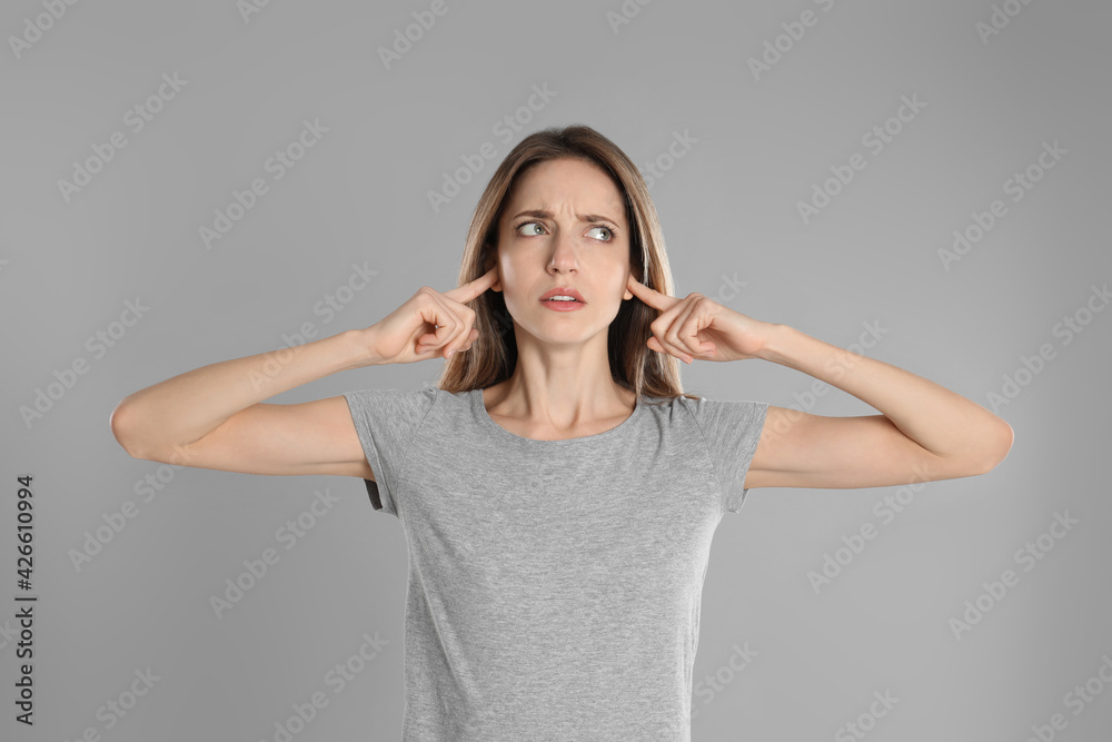 Emotional young woman covering her ears with fingers on grey background Emotional young woman covering her ears with fingers on grey background