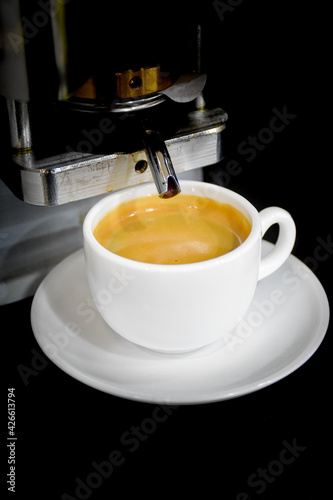 A small espresso coffee cup white with a plate below the espresso machine