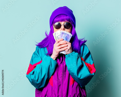 Stylish white girl with purple hair and 80s tracksuit hold cash money on blue background