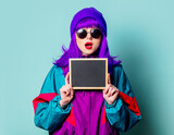 Stylish white girl with purple hair and 80s tracksuit hold board on blue background