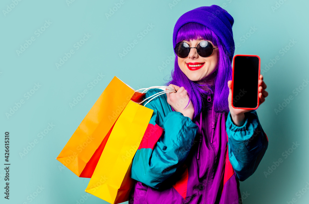 Stylish shopaholic girl in 80s tracksuit and sunglasses hold shopping bags and mobile phone - obrazy, fototapety, plakaty 