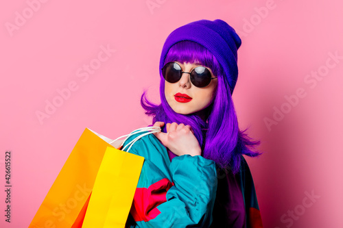 Stylish shopaholic girl in 80s tracksuit and sunglasses hold shopping bags