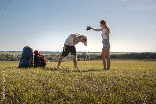 Young cheerful tourist couple with backpacks in the campaign.Young cheerful tourist couple with backpacks in the campaign. The girl pours water on the young man.