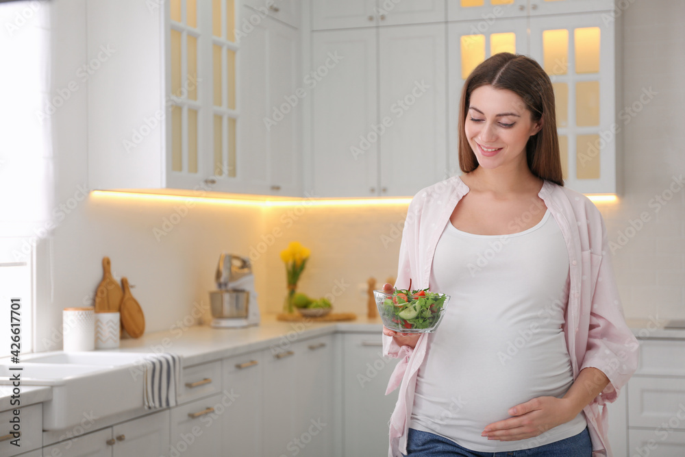 Young pregnant woman with vegetable salad in kitchen, space for text. Healthy eating Young pregnant woman with vegetable salad in kitchen, space for text. Healthy eating