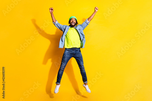Full size photo of young cheerful smiling good mood afro man jumping in victory isolated on yellow color background