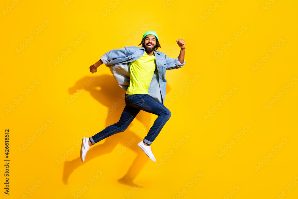 Full size profile photo of optimistic nice brunet man jump wear jacket cap jeans isolated on yellow color background