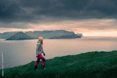 Woman hiking on Kalsoy Island during sunset, coast of island Eysturoy ion background, dramatic sky, Faroe Islands. photo