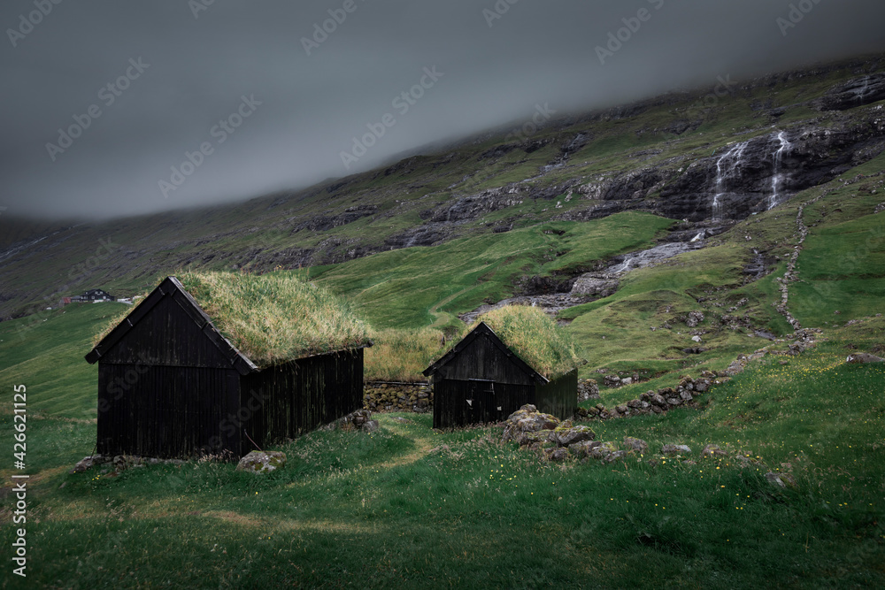 Huts with a grass roof and waterfall in Saksun village on Streymoy Island, dark rain clouds, Faroe Islands. Huts with a grass roof and waterfall in Saksun village on Streymoy Island, dark rain clouds, Faroe Islands.