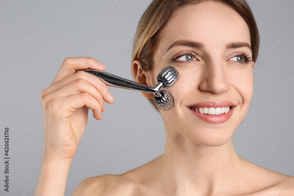 Young woman using metal face roller on light grey background Young woman using metal face roller on light grey background