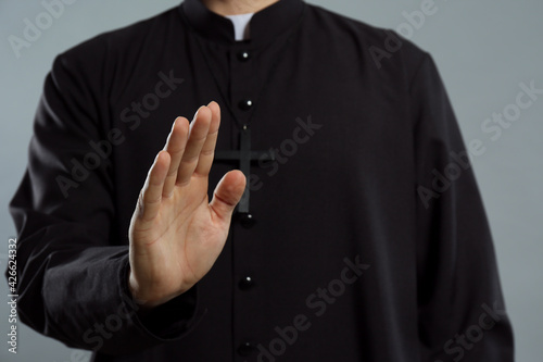 Priest making blessing gesture on grey background, closeup