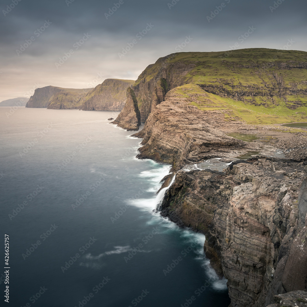 Coast, waterfall and cliffs at Trælanípa on the island of Vagar, by Lake Leitisvatn. Last rays of the sun at sunset.. Coast, waterfall and cliffs at Trælanípa on the island of Vagar, by Lake Leitisvatn. Last rays of the sun at sunset..