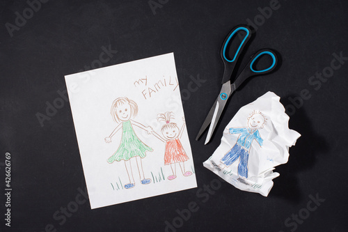 Child's drawing of a family on paper. Mom, dad and baby are holding hands. Family divorce concept. The father's image is cut with scissors. Relationship problems and difficulties