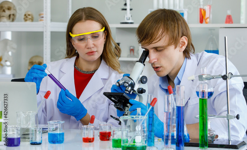 Caucasian man and woman scientist in laboratory. Man scientist look through microscope and woman scientist hold and look at test tube and equipment science are many test tube put on table 