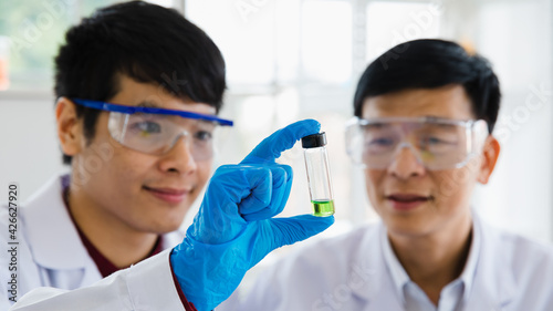 2 Scientist asian adults man wearing eyeglass look at glassware as green liquid in laboratory