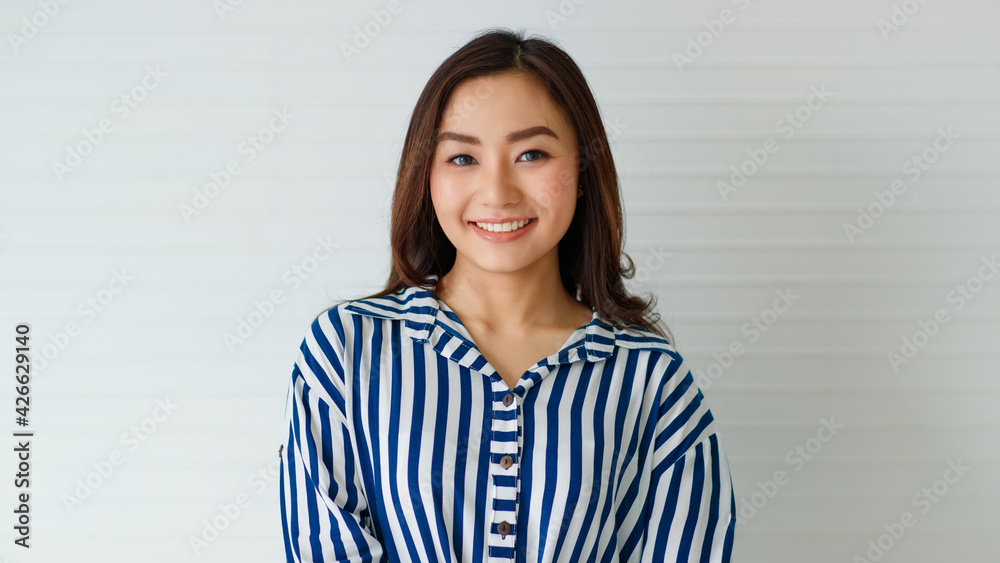 Horizontal half-body portrait shot of a cute smiling Asian woman in casual long sleeve blue and white striped shirt looking at the camera in the studio isolated with white background Horizontal half-body portrait shot of a cute smiling Asian woman in casual long sleeve blue and white striped shirt looking at the camera in the studio isolated with white background