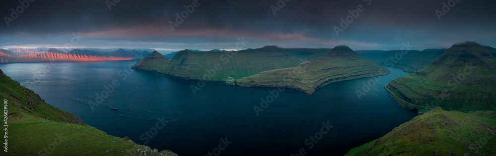 Panoramic view from Hvithamar near the town of Gjogv on the Faroe Island coast of Eysturoy over the green fjord towards Kalsoy at sunset.