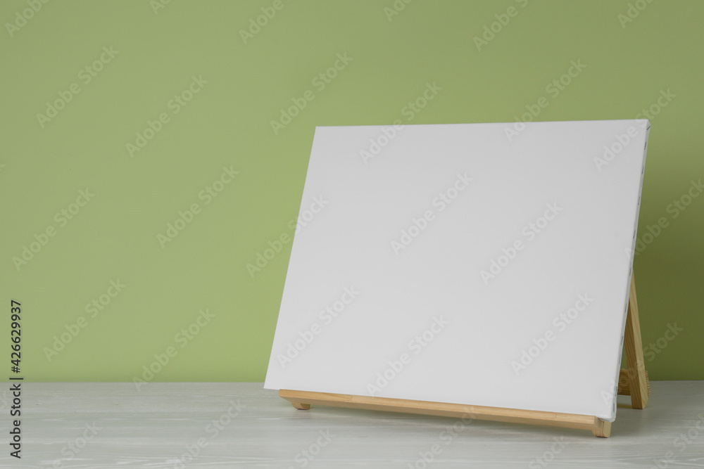 Wooden easel with blank canvas on white table. Space for text Wooden easel with blank canvas on white table. Space for text