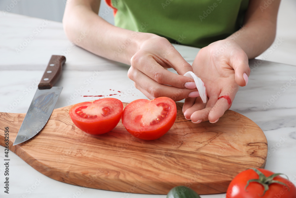 Young woman wiping cut finger with cotton pad in kitchen, closeup Young woman wiping cut finger with cotton pad in kitchen, closeup