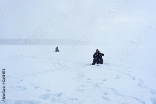 ice fishing with two fishermen on the ice in the process of catching fish. Snowfall © Алексей Филатов