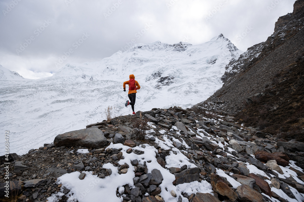 Woman trail runner cross country running up hill to winter snow mountain top