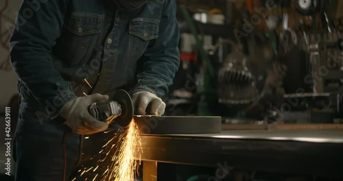 Locksmith in safety face mask sands the edges of a metal detail by electric grinder with a lot of sparks in slow motion, metalwork at workshop, 4k 60p Prores HQ photo