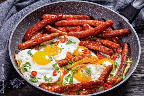 sausages with fried eggs in a pan, top view