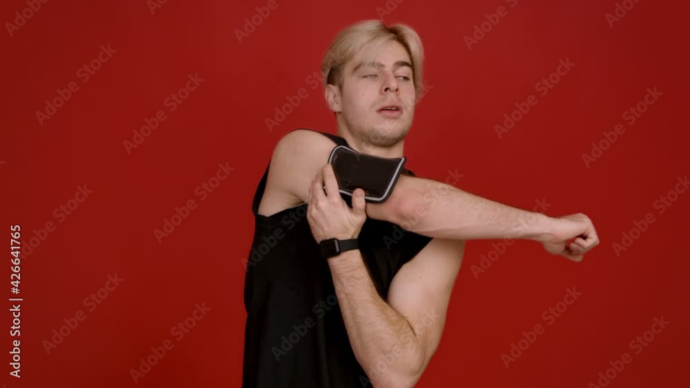 Active young sportsman warming up his muscles, stretching hands before training, red studio background, slow motion Active young sportsman warming up his muscles, stretching hands before training, red studio background, slow motion