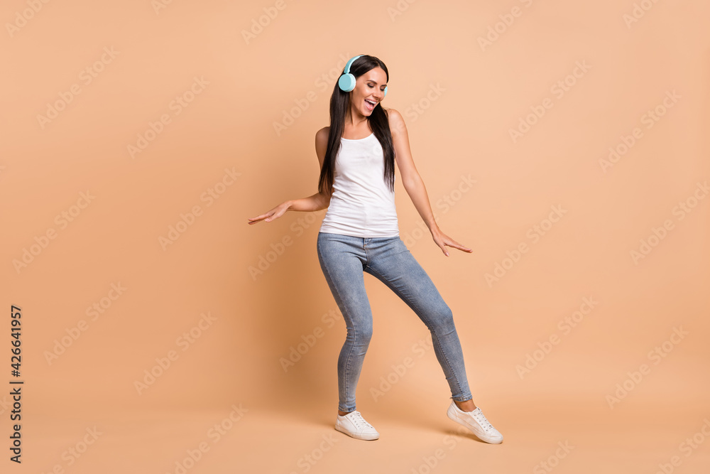 Full length photo portrait of woman in earphones dancing isolated on pastel beige colored background Full length photo portrait of woman in earphones dancing isolated on pastel beige colored background